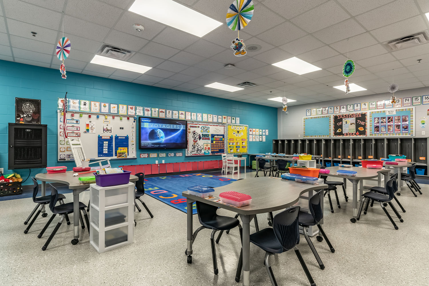 Colorful elementary school classroom with desks, chairs, wall-mounted T.V. and student cubbies